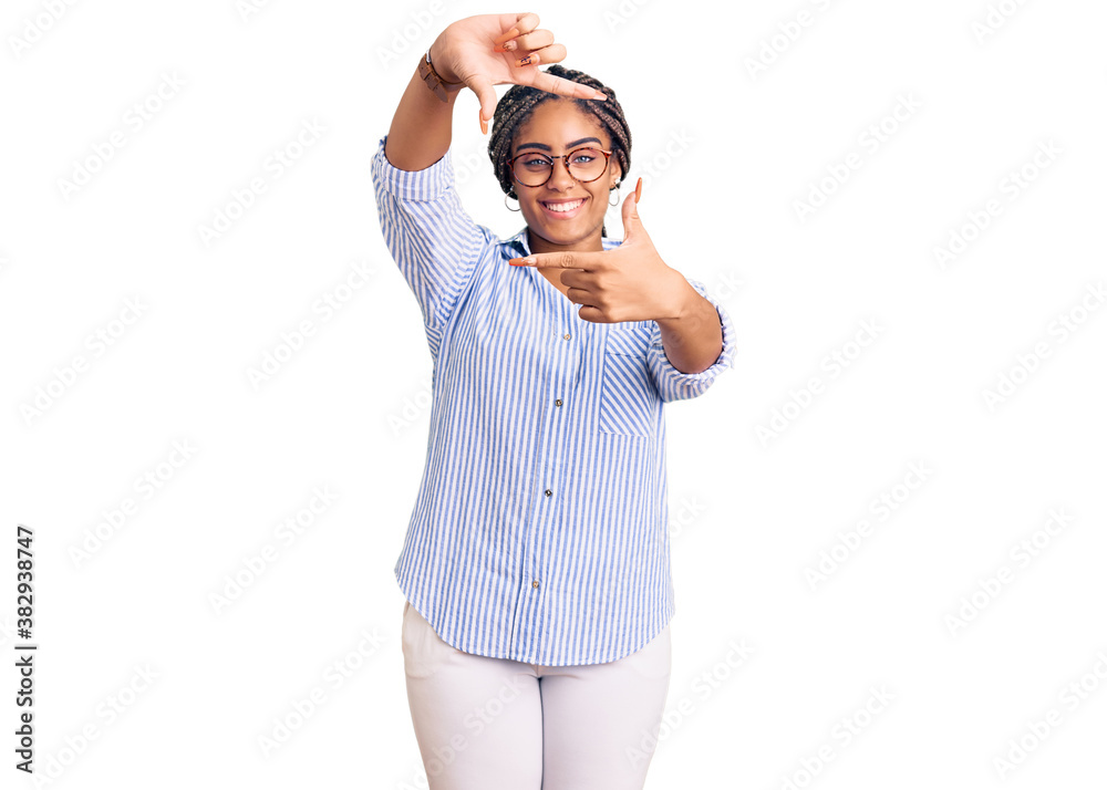 Fototapeta premium Young african american woman with braids wearing casual clothes and glasses smiling making frame with hands and fingers with happy face. creativity and photography concept.