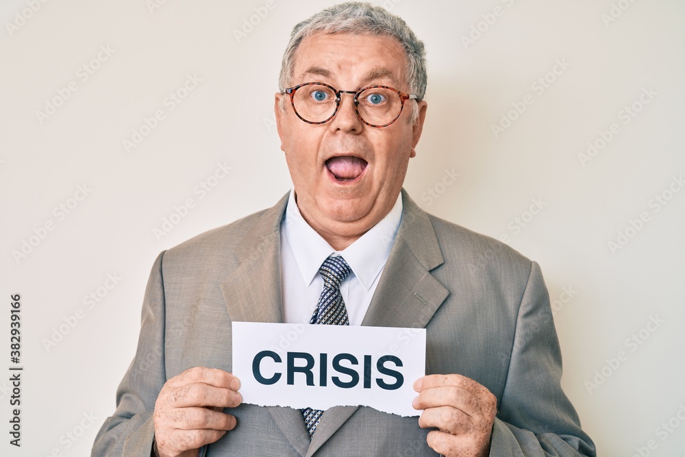 Senior grey-haired man wearing business suit holding crisis paper celebrating crazy and amazed for success with open eyes screaming excited. Senior grey-haired man wearing business suit holding crisis paper celebrating crazy and amazed for success with open eyes screaming excited.