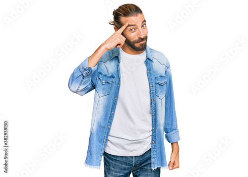 Attractive man with long hair and beard wearing casual denim jacket smiling pointing to head with one finger, great idea or thought, good memory