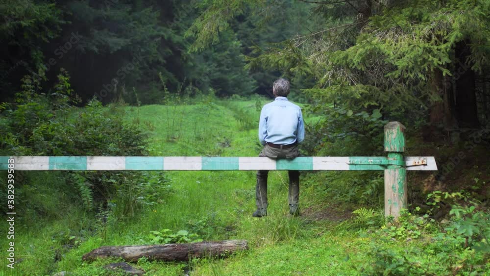 Man sits on a wooden barrier in a spruce forest Man sits on a wooden barrier in a spruce forest