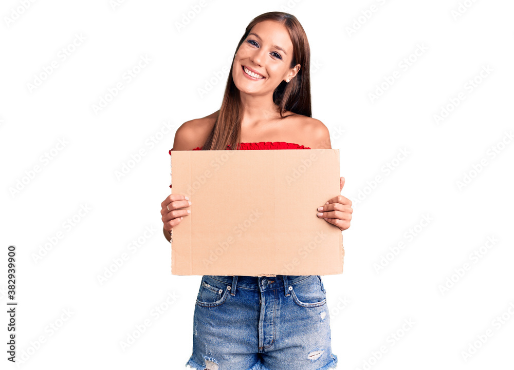 Young beautiful hispanic woman holding banner cardboard looking positive and happy standing and smiling with a confident smile showing teeth Young beautiful hispanic woman holding banner cardboard looking positive and happy standing and smiling with a confident smile showing teeth