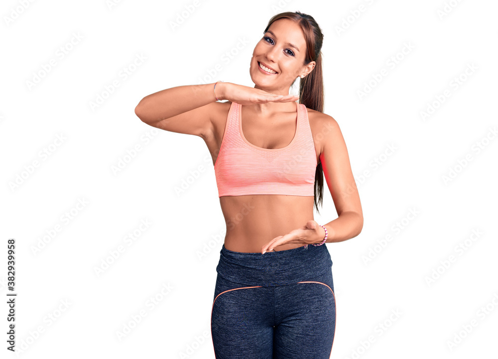 Young beautiful hispanic woman wearing sportswear gesturing with hands showing big and large size sign, measure symbol. smiling looking at the camera. measuring concept. Young beautiful hispanic woman wearing sportswear gesturing with hands showing big and large size sign, measure symbol. smiling looking at the camera. measuring concept.