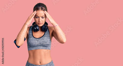 Young beautiful hispanic woman wearing gym clothes and using headphones with hand on head for pain in head because stress. suffering migraine.