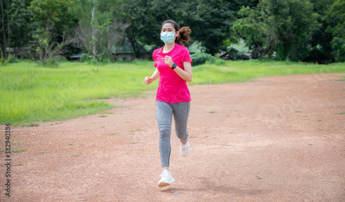 Runner woman running on the trails road while wearing surgical mask. Running on soft surfaces decrease the risk of overuse injuries and reduce impact.