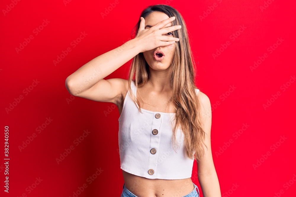 Fototapeta premium Young beautiful girl wearing casual sleeveless t-shirt peeking in shock covering face and eyes with hand, looking through fingers afraid