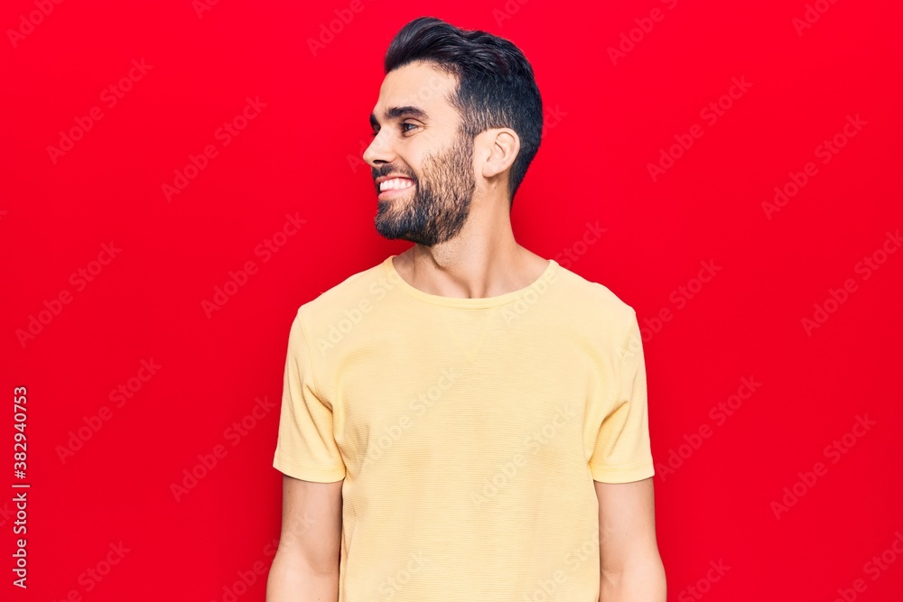 Young handsome man with beard wearing casual t-shirt looking away to side with smile on face, natural expression. laughing confident. Young handsome man with beard wearing casual t-shirt looking away to side with smile on face, natural expression. laughing confident.