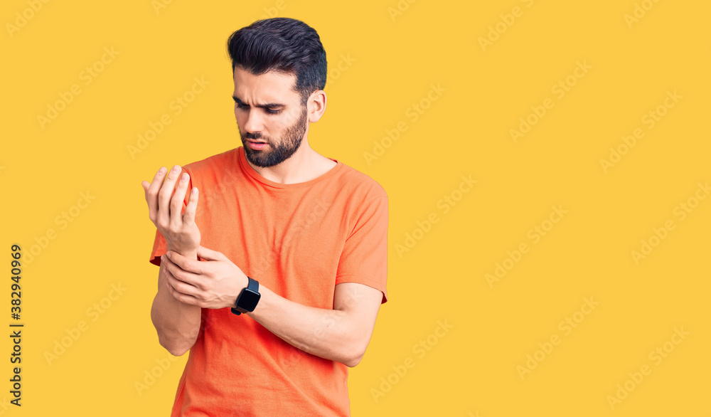 Young handsome man with beard wearing casual t-shirt suffering pain on hands and fingers, arthritis inflammation Young handsome man with beard wearing casual t-shirt suffering pain on hands and fingers, arthritis inflammation