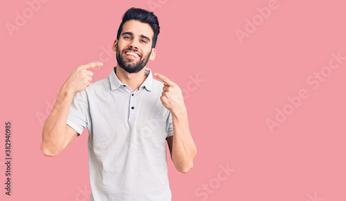 Young handsome man with beard wearing casual polo smiling cheerful showing and pointing with fingers teeth and mouth. dental health concept. © Krakenimages.com