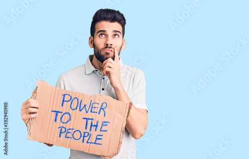 Young handsome man with beard holding power to the people cardboard banner serious face thinking about question with hand on chin, thoughtful about confusing idea photo