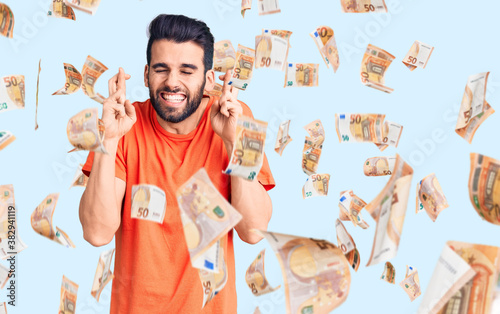 Young handsome man with beard wearing casual t-shirt gesturing finger crossed smiling with hope and eyes closed. luck and superstitious concept. photo