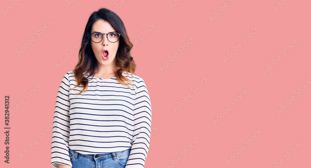 Obraz premium Beautiful young brunette woman wearing casual clothes and glasses afraid and shocked with surprise expression, fear and excited face.