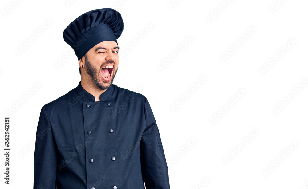 Young hispanic man wearing cooker uniform winking looking at the camera with sexy expression, cheerful and happy face. Young hispanic man wearing cooker uniform winking looking at the camera with sexy expression, cheerful and happy face.