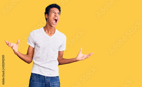 Young african american man wearing casual white t shirt crazy and mad shouting and yelling with aggressive expression and arms raised. frustration concept.