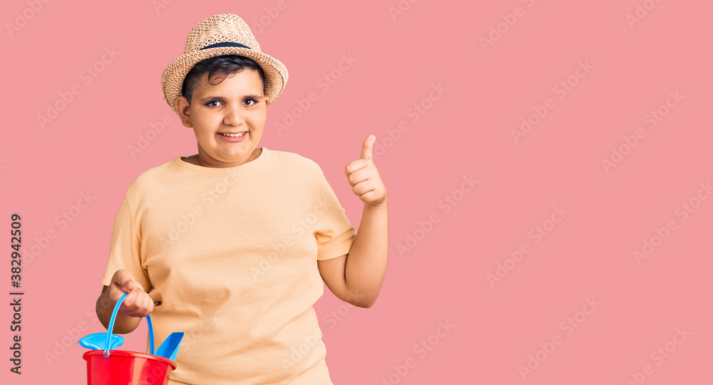 Little boy kid playing with summer shovel and bucket toys smiling happy and positive, thumb up doing excellent and approval sign Little boy kid playing with summer shovel and bucket toys smiling happy and positive, thumb up doing excellent and approval sign