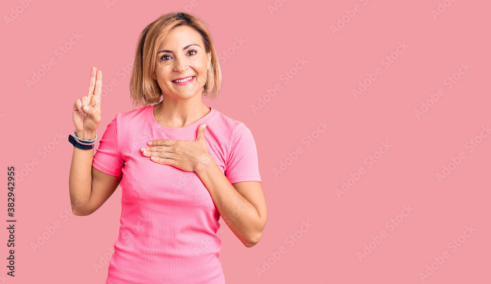Young blonde woman wearing sportswear smiling swearing with hand on chest and fingers up, making a loyalty promise oath Young blonde woman wearing sportswear smiling swearing with hand on chest and fingers up, making a loyalty promise oath