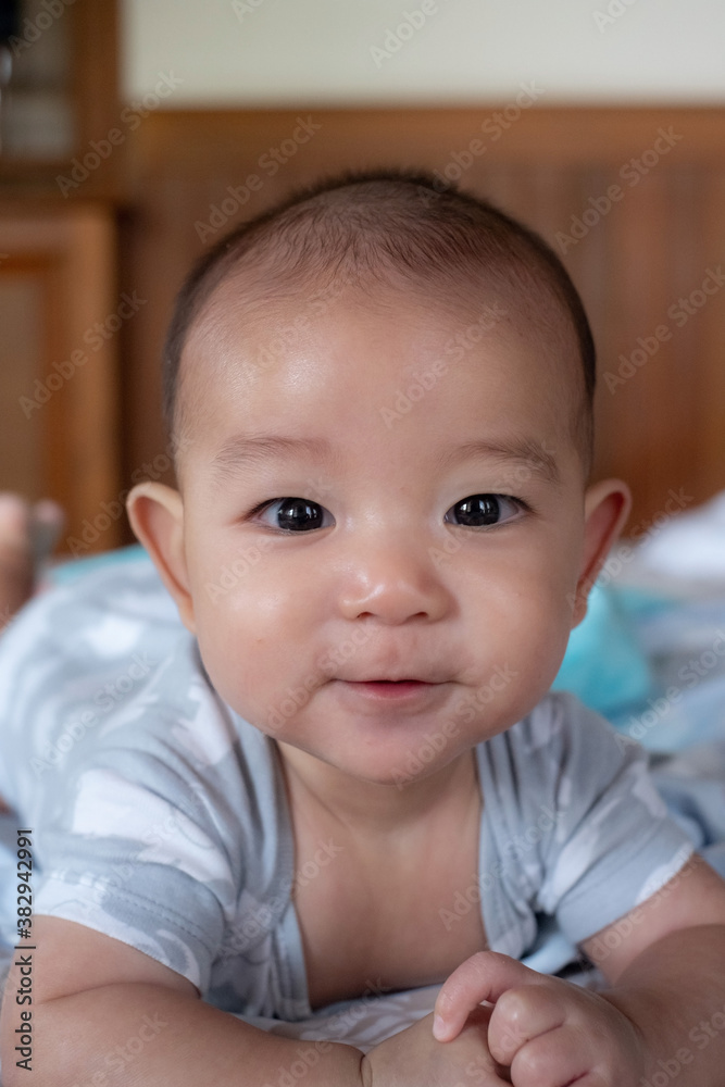 Portrait of happy small Asian infant baby. Kid is lying, smiling, playing on the bed