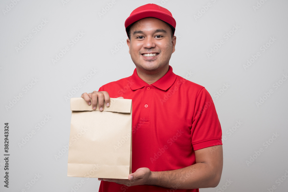 Young smiling asian delivery man in red uniform holding paper bag food