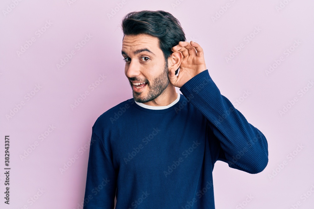 Young hispanic man wearing casual clothes smiling with hand over ear listening and hearing to rumor or gossip. deafness concept. Young hispanic man wearing casual clothes smiling with hand over ear listening and hearing to rumor or gossip. deafness concept.