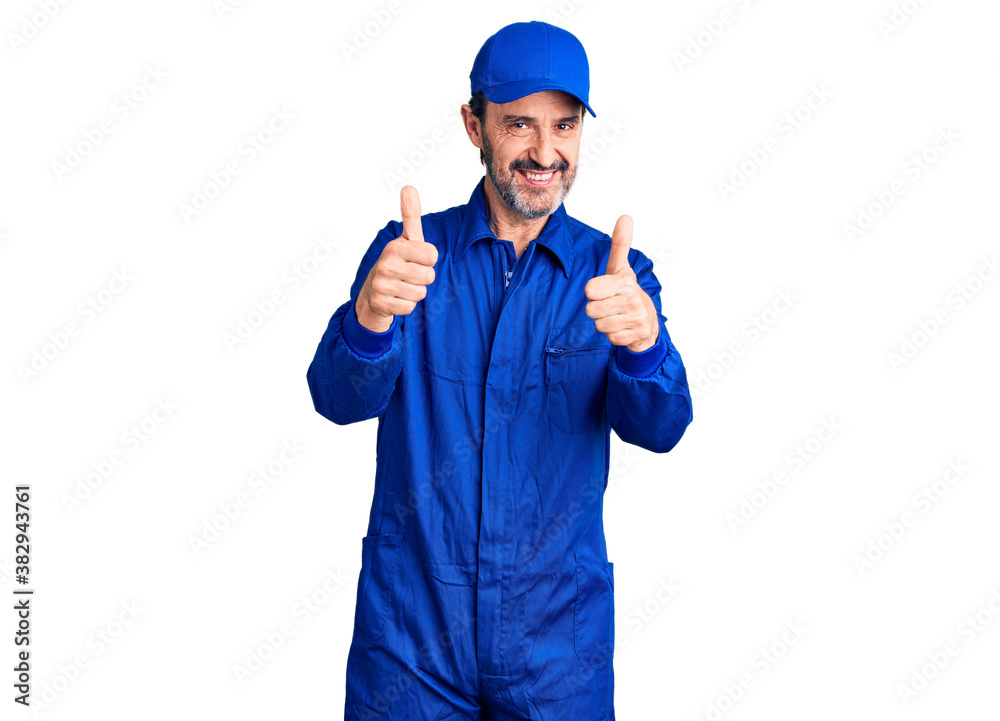 Middle age handsome man wearing mechanic uniform success sign doing positive gesture with hand, thumbs up smiling and happy. cheerful expression and winner gesture.