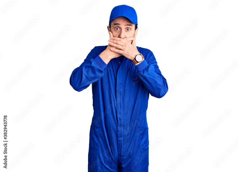 Middle age handsome man wearing mechanic uniform shocked covering mouth with hands for mistake. secret concept.