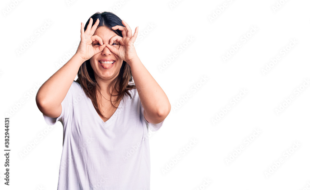 Young beautiful brunette woman wearing casual t-shirt doing ok gesture like binoculars sticking tongue out, eyes looking through fingers. crazy expression. Young beautiful brunette woman wearing casual t-shirt doing ok gesture like binoculars sticking tongue out, eyes looking through fingers. crazy expression.