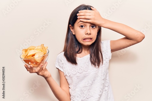 Beautiful child girl holding potato chip stressed and frustrated with hand on head, surprised and angry face