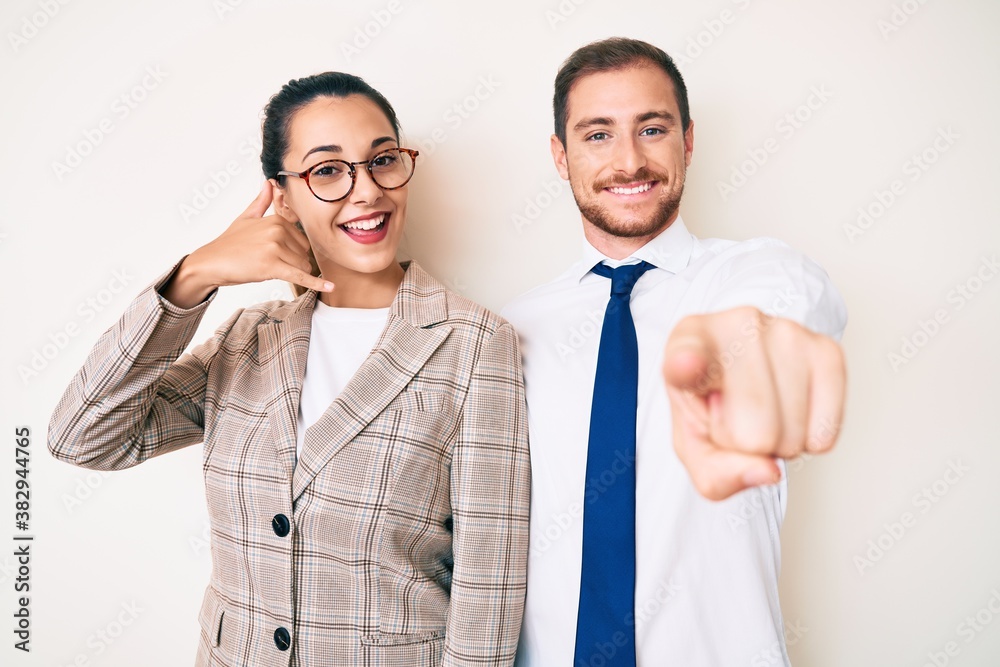 Beautiful couple wearing business clothes smiling doing talking on the telephone gesture and pointing to you. call me. Beautiful couple wearing business clothes smiling doing talking on the telephone gesture and pointing to you. call me.