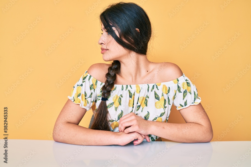 Brunette teenager girl wearing casual clothes sitting on the table looking to side, relax profile pose with natural face with confident smile. Brunette teenager girl wearing casual clothes sitting on the table looking to side, relax profile pose with natural face with confident smile.