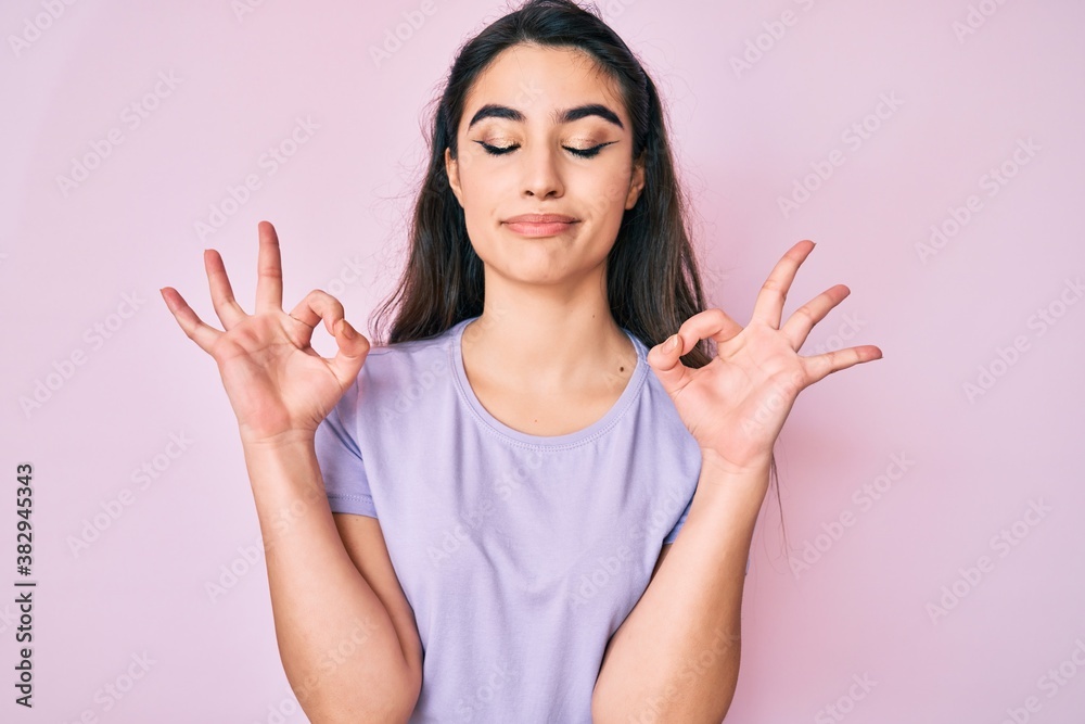 Brunette teenager girl wearing casual clothes relax and smiling with eyes closed doing meditation gesture with fingers. yoga concept. Brunette teenager girl wearing casual clothes relax and smiling with eyes closed doing meditation gesture with fingers. yoga concept.