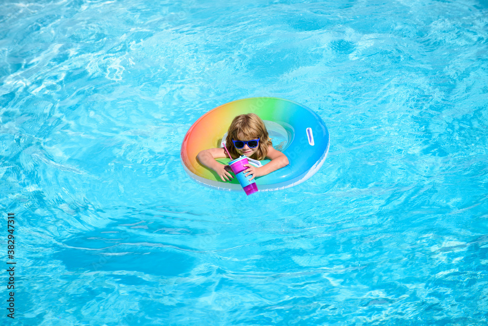 Cute funny little toddler boy in a colorful swimming suit and sunglasses relaxing with toy ring floating in a pool having fun during summer vacation in a tropical resort. Panorama blue sea wave.