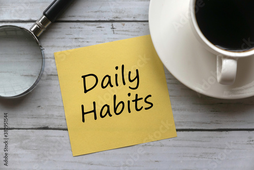 Canvas-taulu Top view of a cup of coffee, magnifying glass and yellow memo note written with daily habits on white wooden background
