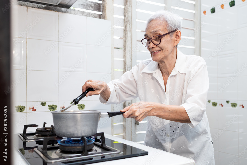 Old elderly people cooking vegetables soup,mixing and heating the ingredients,healthy food,good cook,asian senior woman standing by the stove in the kitchen at home,preparing food,concoction concept.
