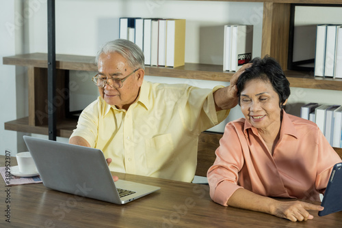 Senior Asian elderly couple in home casual outfit with happy smiling emotion sitting in living room using laptop and tablet together