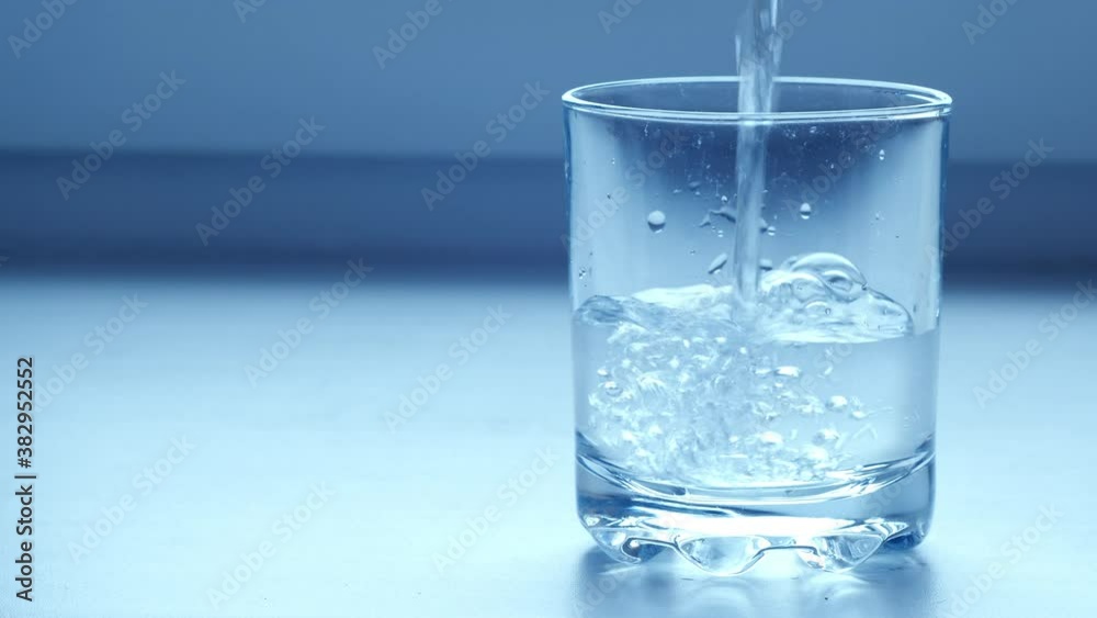 Clear drinking water pouring into glass on blue grey background. Mineral water pouring into transparent glass on bright background Clear drinking water pouring into glass on blue grey background. Mineral water pouring into transparent glass on bright background