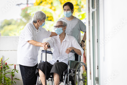 Happy asian senior woman wearing protective mask sit in wheelchair with best friend visit to the home during COVID-19,Coronavirus pandemic,old elderly people embracing holding hands warm relations