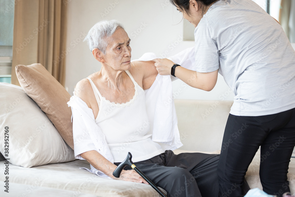 Asian female caregiver taking care of helping elderly patient get dressed,wearing clothes or undressing for senior mother,depressed old woman with amnesia,loss of memory,daily life in a nursing home