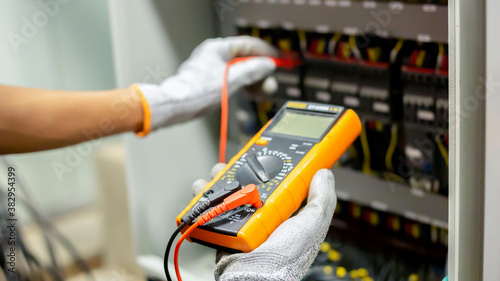 Electrician engineer uses a multimeter to test the electrical installation and power line current in an electrical system control cabinet.