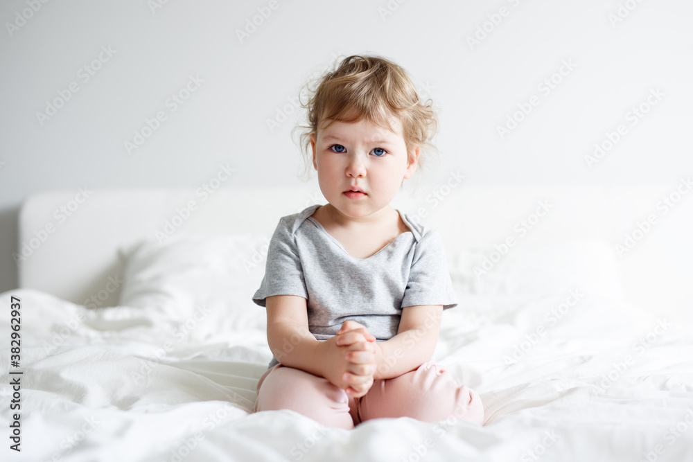 portrait of sad cute little girl sitting on bed portrait of sad cute little girl sitting on bed