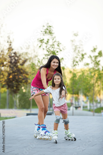beautiful mother and her little daughter rollerskating in park