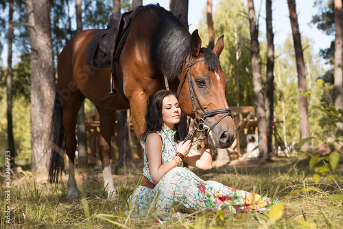Young beautiful woman sitting on the grass in the forest and tenderly hugging her horse  © fotodiya83