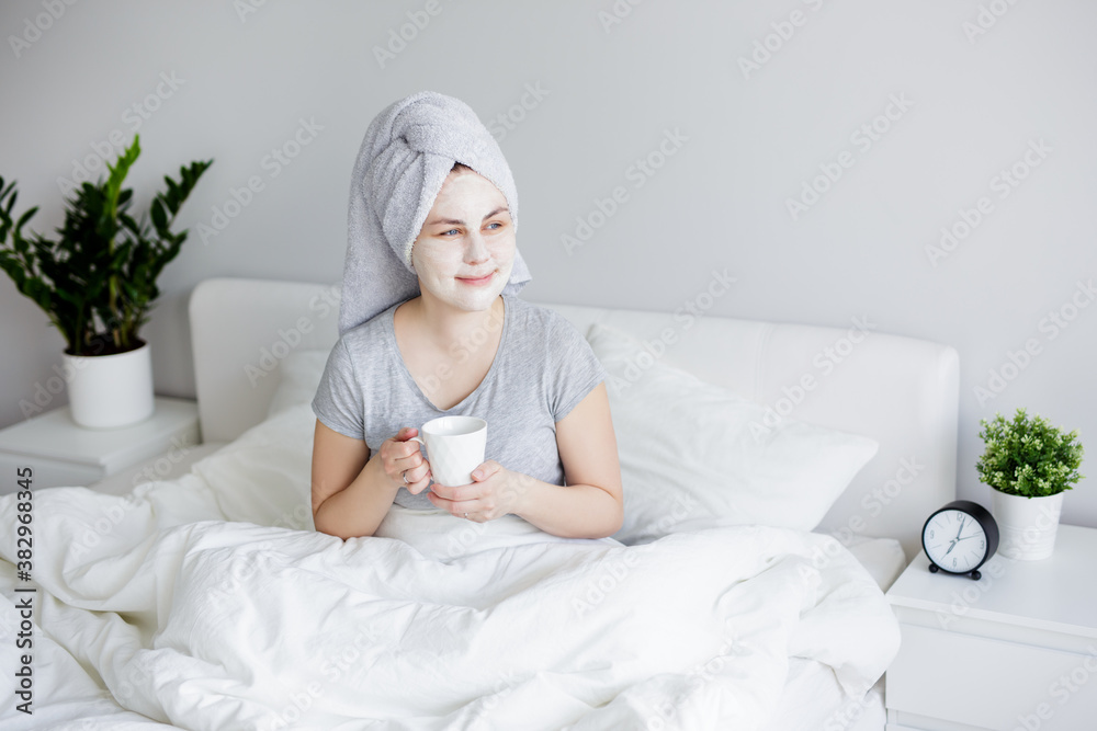 good morning and skin care concept - portrait of woman with facial mask sitting in bed and drinking coffee good morning and skin care concept - portrait of woman with facial mask sitting in bed and drinking coffee