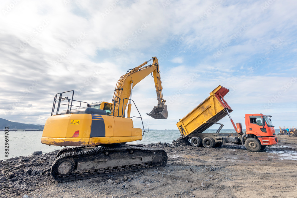 The dump truck is unloading to excavation to sea for filling and an excavator. The dump truck is unloading to excavation to sea for filling and an excavator.