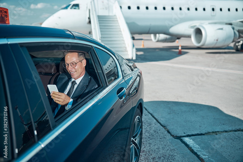 Cheerful businessman with smartphone in car at airport photo