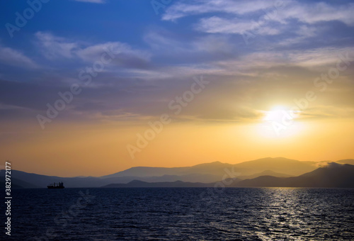 cargo ship travels at sunset © ACHILLEFS