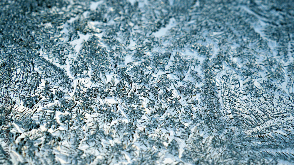 Obraz premium A pattern of ice crystals close-up on a window glass. Blue winter background or wallpaper. Frozen water. Backdrop for Christmas or New Year. Weather forecast: frost, cold snap. Strong macro