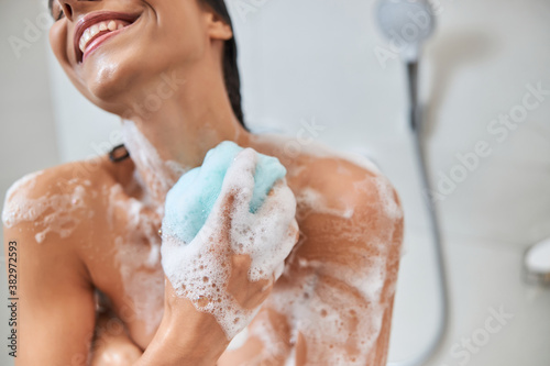 Фотография Smiling young woman using bath loofah while taking shower