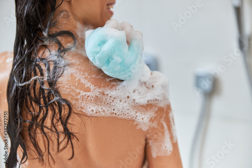 Young woman washing body with blue shower loofah photo