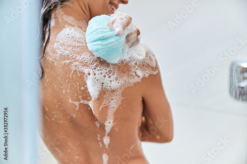 Foto Smiling young woman washing body with blue shower loofah