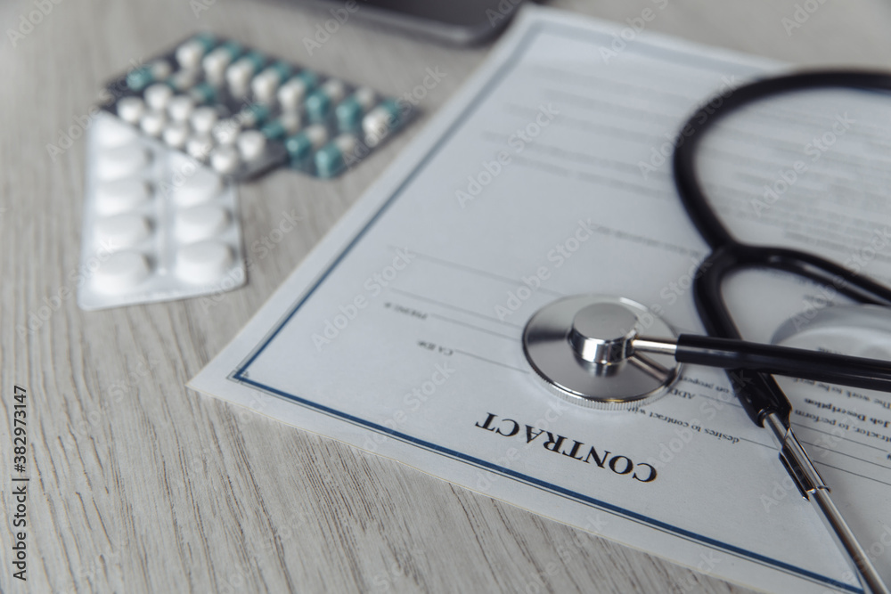 Modern doctor's office desk. Stethoscope and healthcare contract on wooden table close-up.