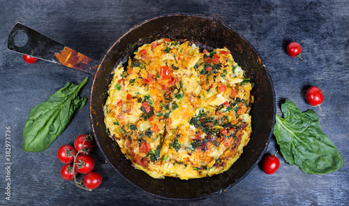 Scrambled eggs with tomatoes and spinach on rustic pan